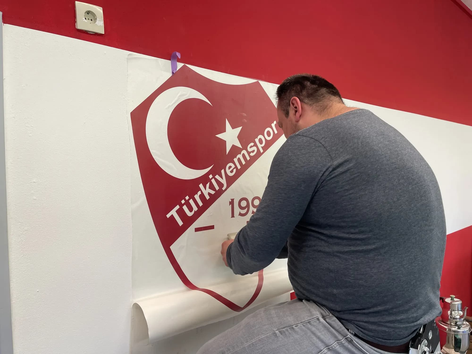 Folierer bringt das rot-weiße Vereinswappen von Türkiyemspor als Wandfolie an